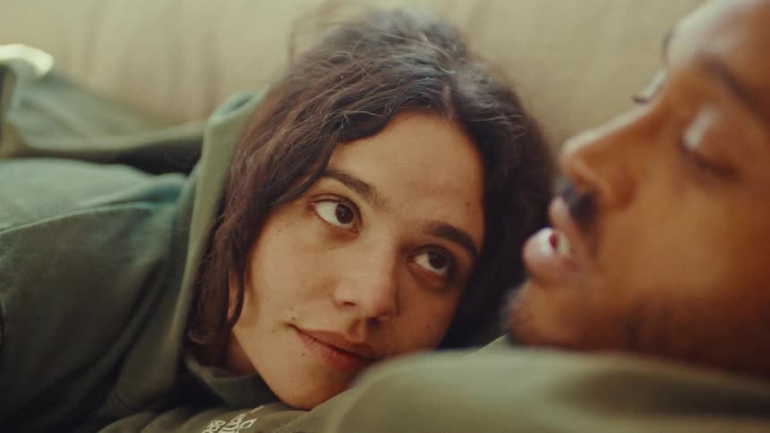 A young couple are cuddling and talking on a bed or couch in a room