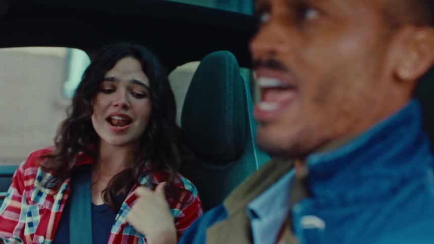 A happy couple are sitting inside a vehicle traveling in a busy city singing and gesturing