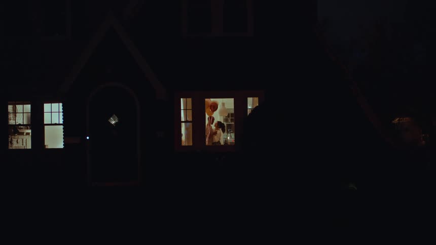 A couple dancing indoors and holding hands at night in their living room
