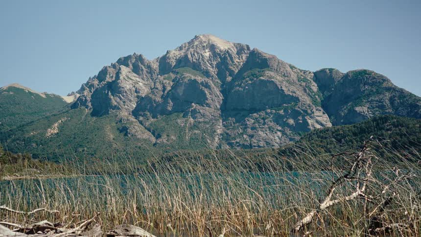 A mountain range surrounded by grass and a lake on the side at midday