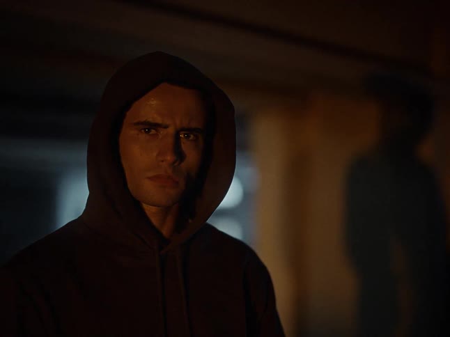 Man wearing a hood in a dark environment with a shadow cast on the wall