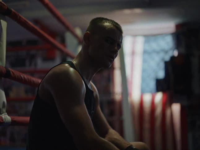 A sweaty man sits on the edge of a boxing ring while resting