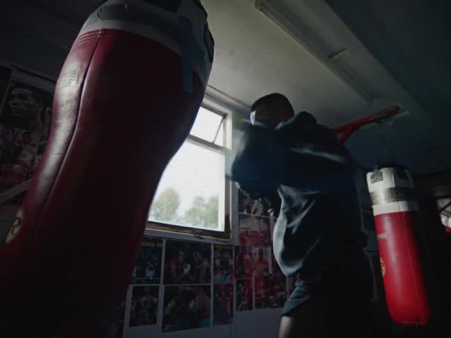 Male boxer trains with the punching bag in the gym during the daytime