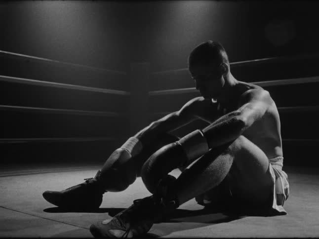 A boxer sits on the floor of a boxing ring looking depressed