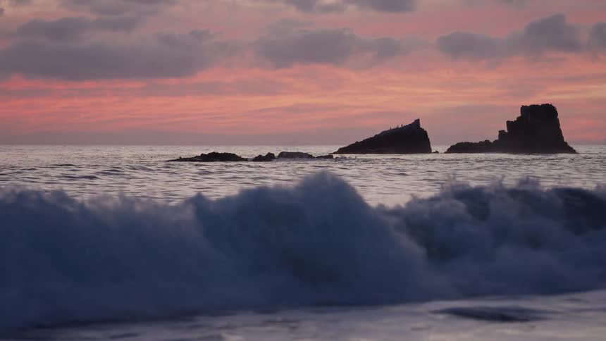 Rocks in the water off the coast as waves splash rolling in to shore