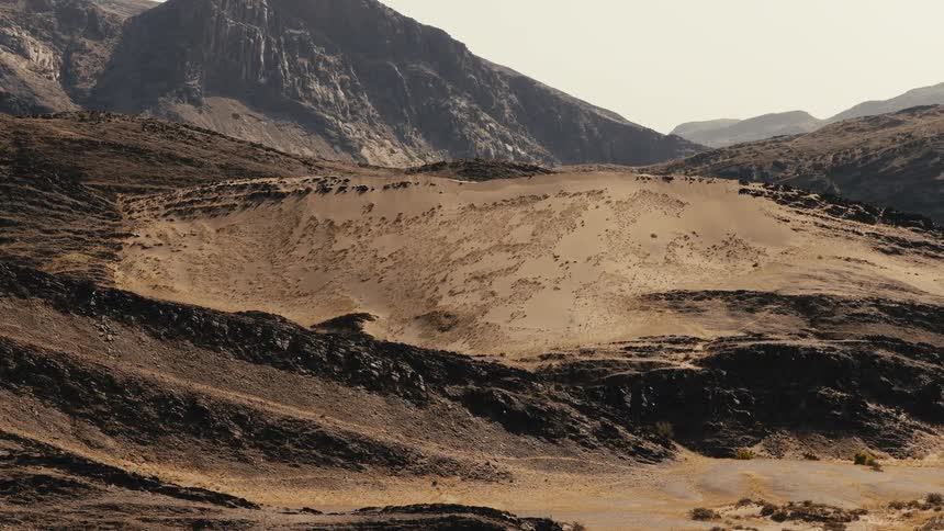 A hill in the wilderness surrounded by a mountain range at midday