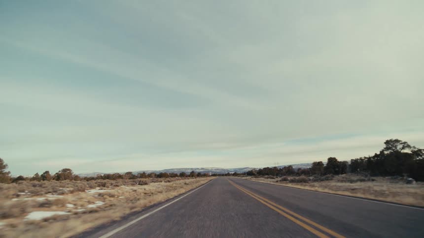 A two lane highway stretching through a vast desert toward distant mountains under a pale blue sky