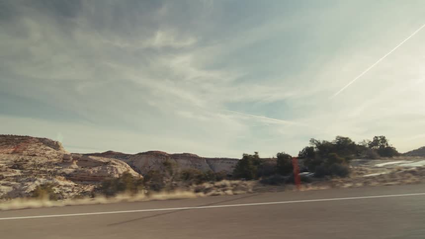 A side view from a moving vehicle captures a desert landscape with mountains and sparse vegetation under a cloudy sky