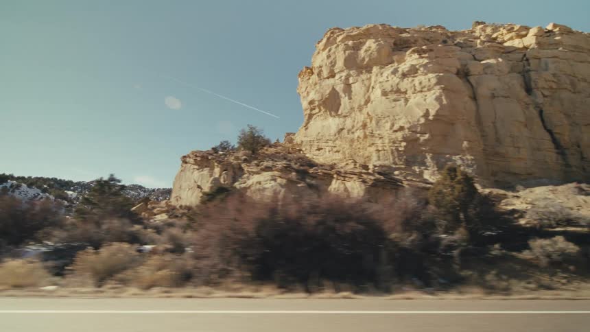 Traveling along a roadway that passes by rocky mountains and plateaus