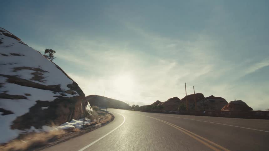 A paved highway as it winds through a desert canyon filled with red rock formations sparse greenery and patches of snow