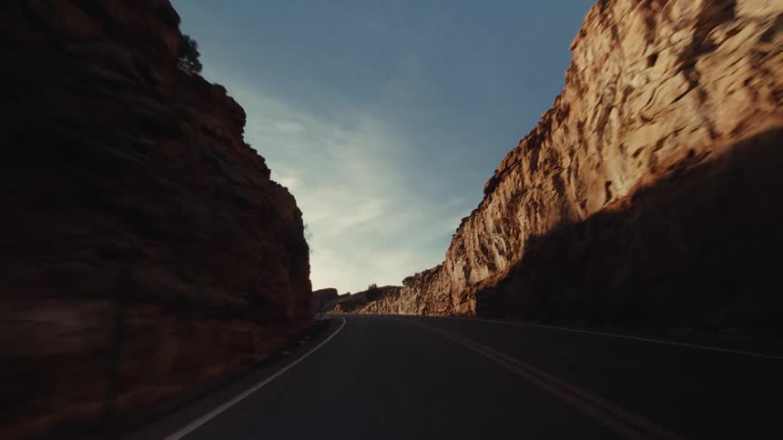 A paved highway as it winds through a desert canyon filled with red rock formations sparse greenery and patches of snow