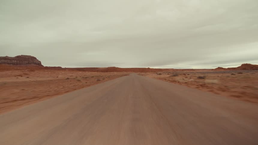 A remote road runs through a desert plain on a cloudy day