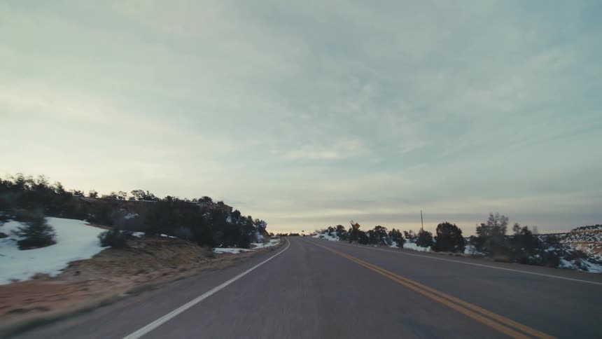 A road trip in the countryside at midday on a winter day with snow covering the sides of the road