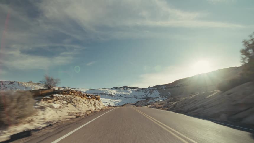 Traveling on a road through mountains with snow on the slopes as the sun shines brightly in the distance