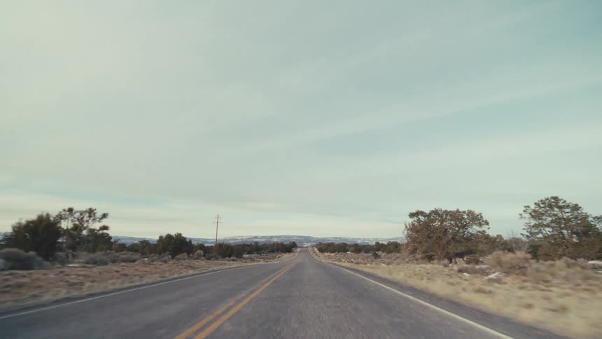 A straight asphalt road cutting through a vast desert valley under a pale sky