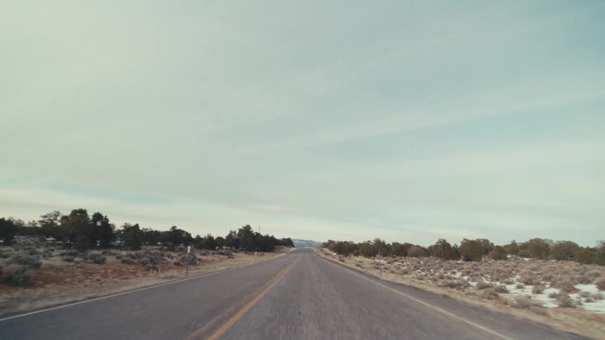 A straight asphalt road cutting through a vast desert valley under a pale sky