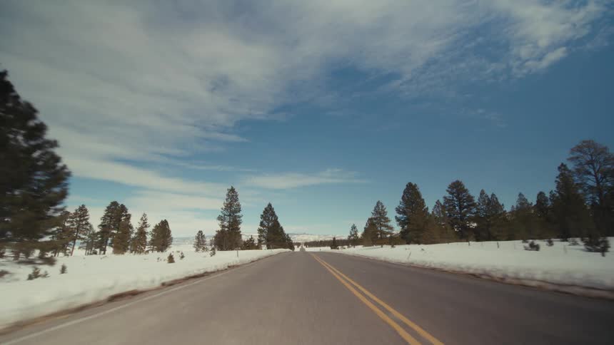 Traveling on a rural road with snow and trees on the roadside and mountains in the distance