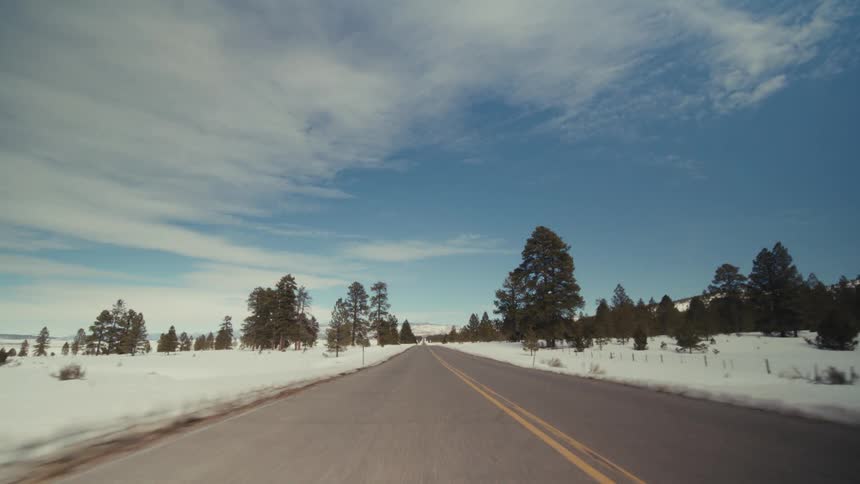 Traveling on a rural road with snow and trees on the roadside and mountains in the distance