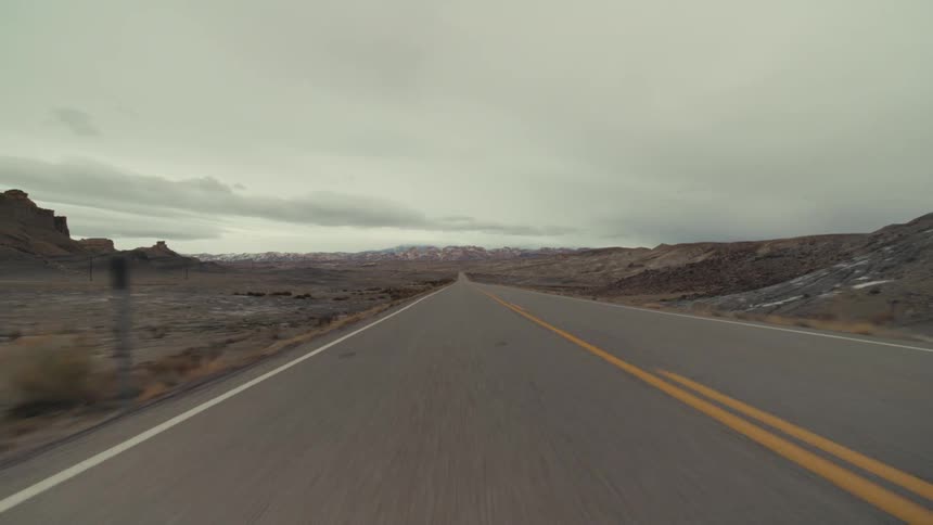 Rural highway crossing through the desert passes mountains and hills on a cloudy day