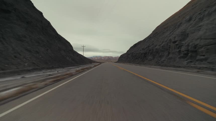 Rural highway crossing through the desert passes mountains and hills on a cloudy day