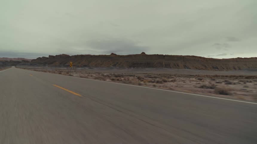 A long highway road passes through a arid landscape with hills