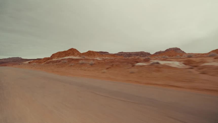 Rural highway passes through arid terrain near the mountains on an overcast day