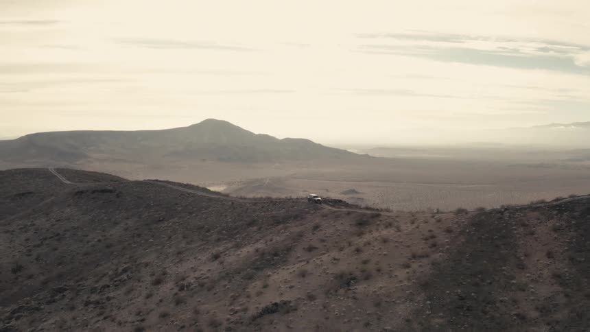 A vehicle drives along a dirt trail that runs across a mountain ridge