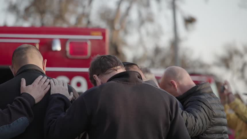 A group of people are gathered to pray near a red fire engine