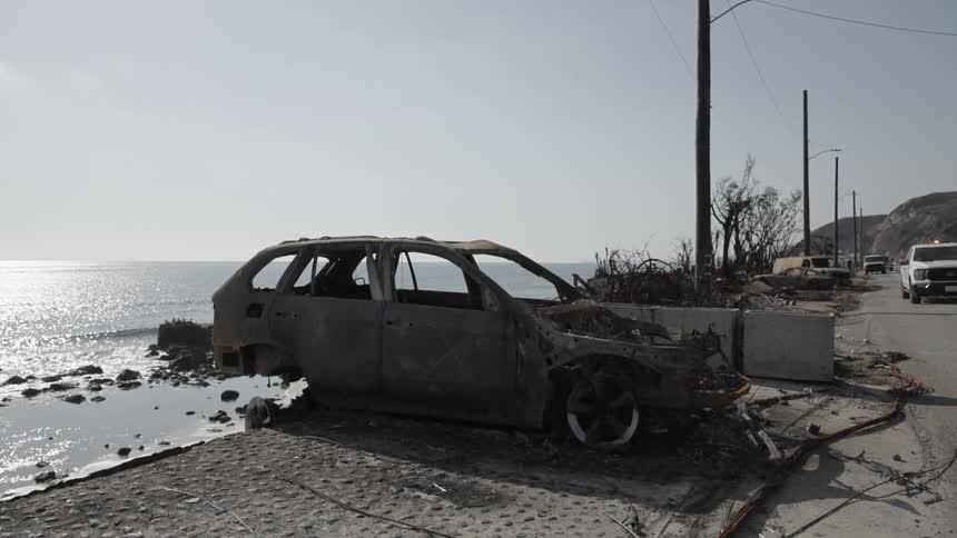 A burned out sedan is parked on an ocean coast on a sunny day