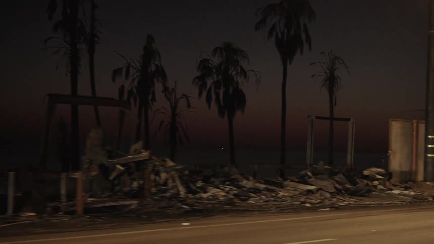 A roadway is lined with debris and damaged trees after a storm