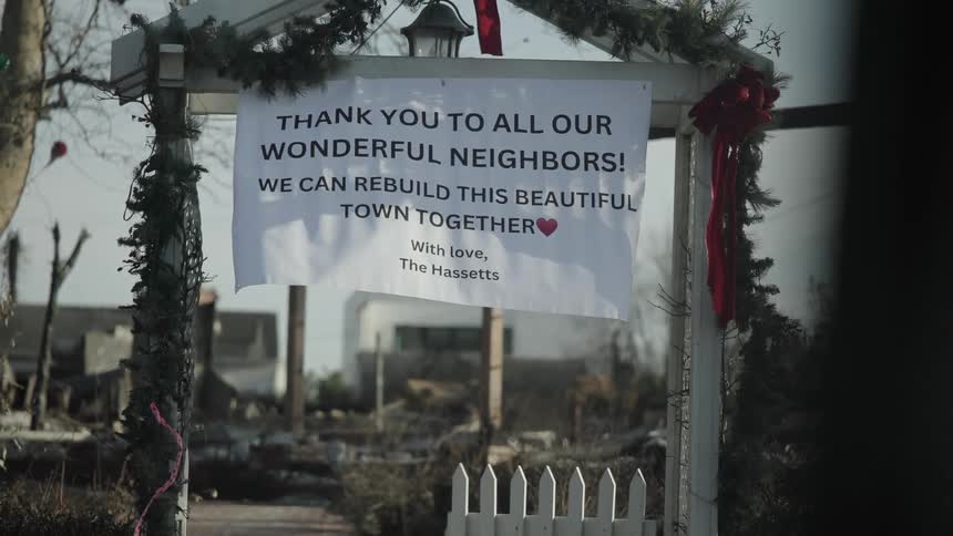 The video displays a hopeful banner hung over a white wooden archway amidst a scene of significant destruction it conveys a message of gratitude to neighbors and a shared commitment to rebuilding the community together