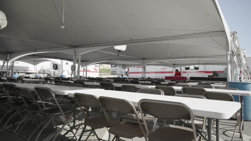 A large tent with rows of folding tables and chairs setup for an event at daytime