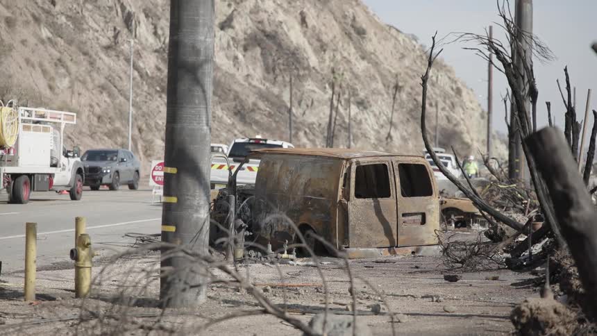 Road construction crew works near a mountain and a rusted van body