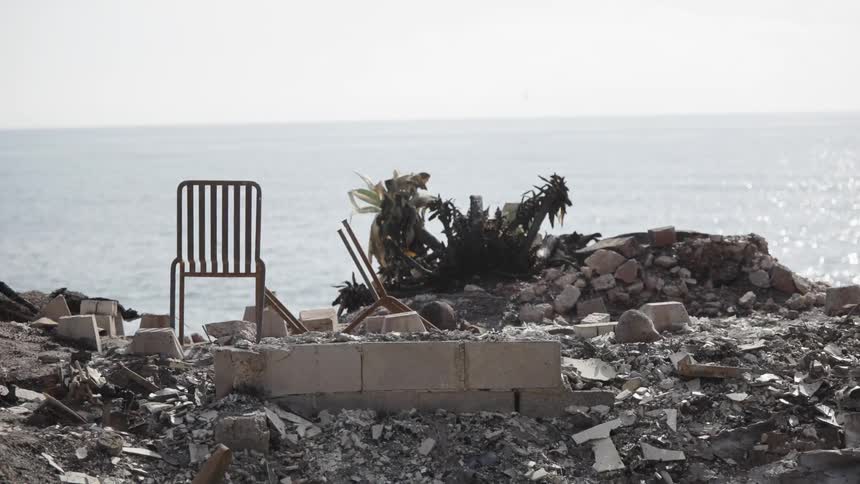 The video shows a desolate scene of rubble and debris overlooking a body of water a lone chair sits among the ruins creating a stark contrast against the calm horizon