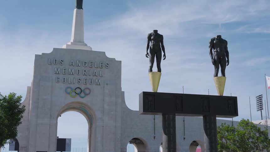 Arch of the los angeles memorial coliseum with olympic rings and statues on pedestals in the foreground