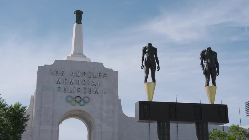 Entrance of the los angeles memorial coliseum with white monument olympic rings and two statues on pedestals