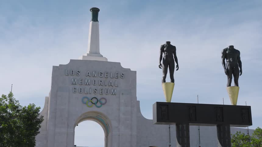 Sculptures stand near an arch of the los angeles memorial coliseum during the daytime
