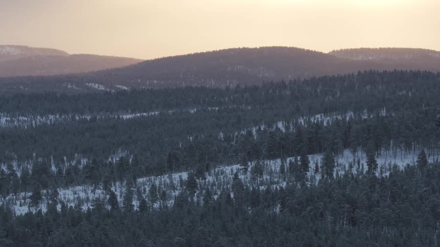 Snow on forested mountains across the landscape under a hazy sky