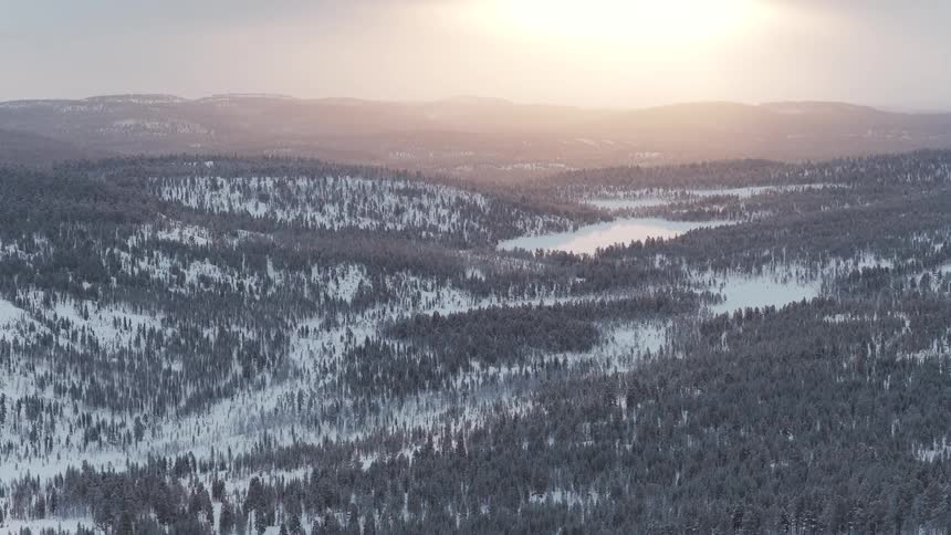 Bright sun shines onto snowy forested hills on a hazy day