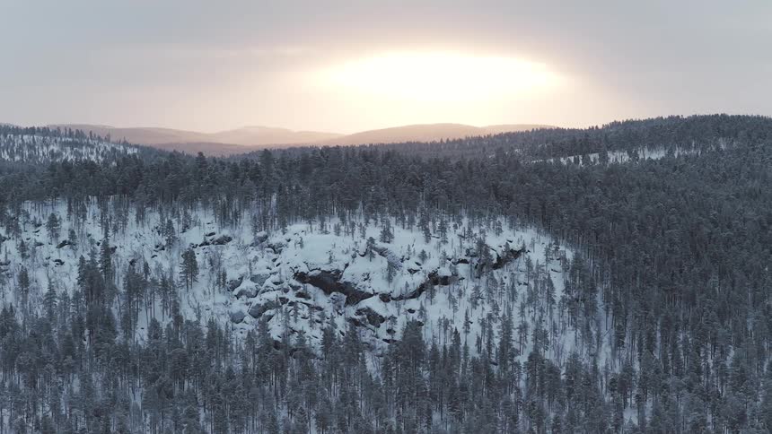 Hills covered by snowcovered forest with exposed rock formation at the center under a sky lit by sunset