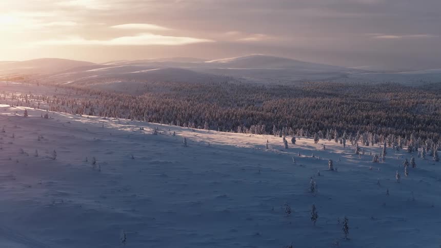 Sun shines from a red sky onto a forested valley and nearby snowy hills