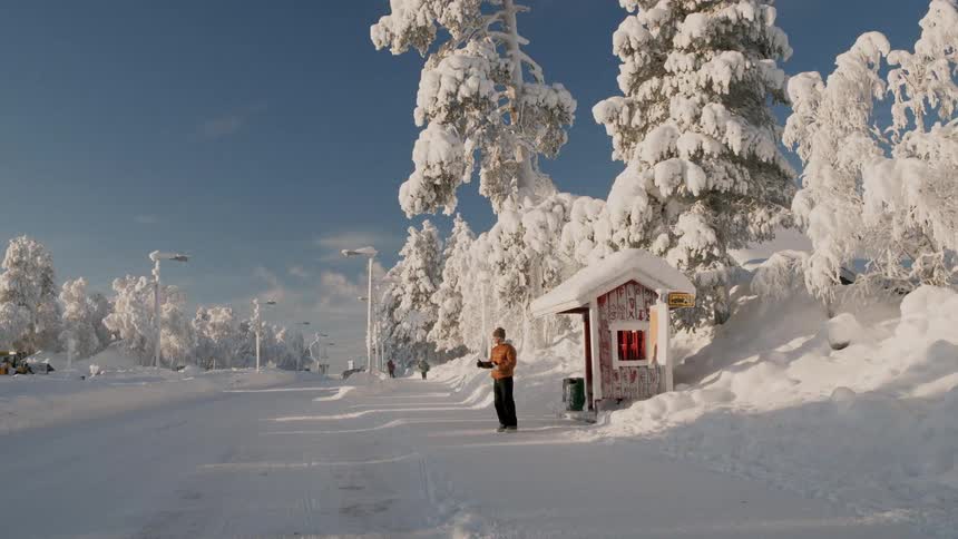 Person standing on snow near a small shelter surrounded by icecovered trees under a blue sky