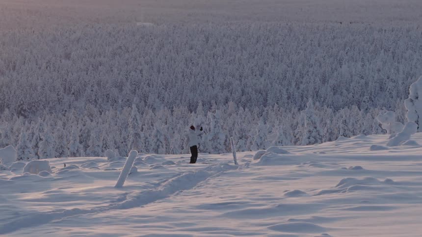 Person walking on a mountain overlooking a snow covered forest holding their phone
