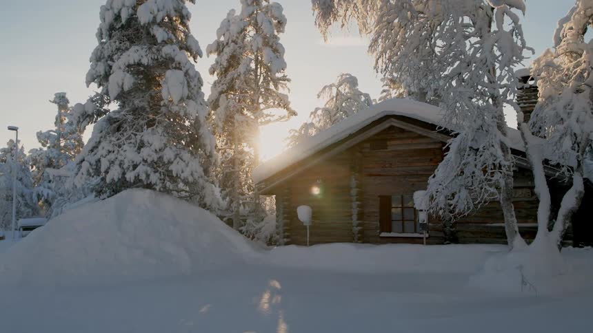 A rustic wooden cabin sits nestled amongst snowcovered trees as the sun shines through the branches illuminating the winter landscape