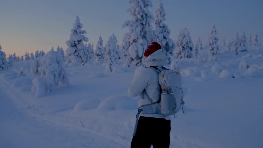 Woman wearing a backpack walks on a mountain with snow covered trees
