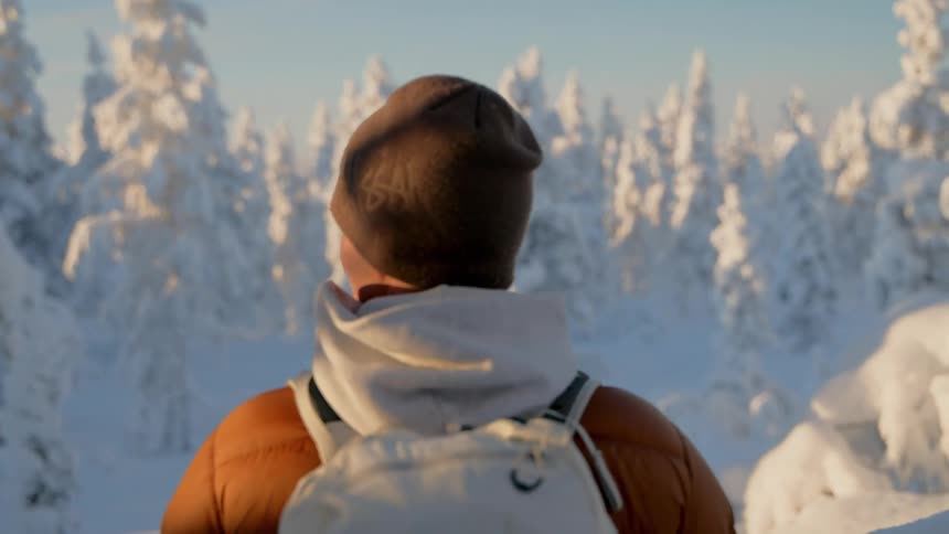 Person with a backpack looks at a snowcovered forest under a clear sky