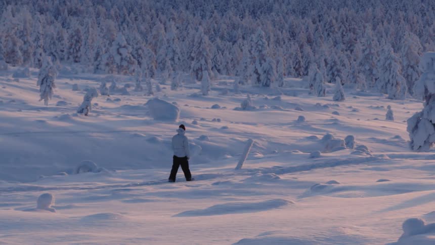 A lone hiker walks across a snow covered landscape near a forest