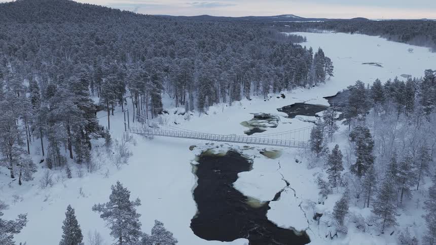 Bridge crosses a partially frozen river winding past frost covered forest on a winter day