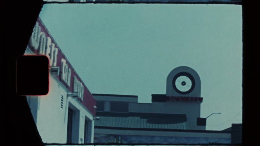The video displays a vintage filmstyle shot of an urban building exterior under a clear sky a prominent circular sign featuring a targetlike design is visible atop the structure accompanied by red lettering along the roofline