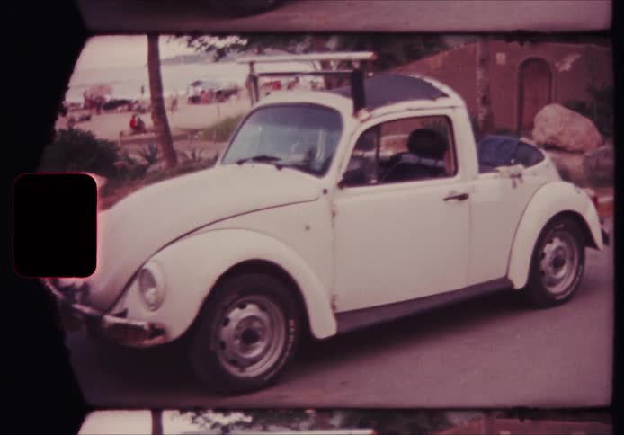 White volkswagen beetle parked near the beach with a motorcycle in the background